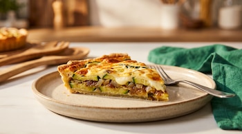 Porción de tarta de zapallitos y queso sobre un plato claro junto a un tenedor de metal y una servilleta verde.