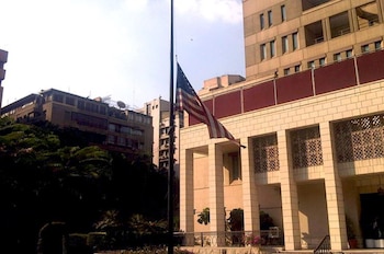 Exterior de la Embajada de Estados Unidos en El Cairo con la bandera estadounidense a media asta y edificios al fondo bajo un cielo claro