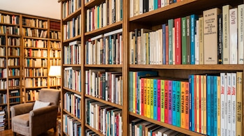 Estanterías de madera con libros de Roland Barthes, Bajtín, Mafalda, Tintín y Astérix, un sillón y una lámpara encendida al fondo.