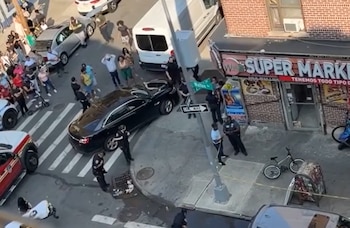 Vista aérea de una calle urbana con vehículos, una multitud de personas, agentes de policía, un supermercado y bicicletas estacionadas
