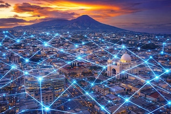 Vista aérea de una ciudad al anochecer con edificios iluminados, volcán al fondo y cielo vibrante. Una red de luces azules brillantes se superpone a la urbe.
