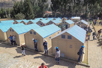 Filas de refugios prefabricados de color beige con techos azules y el logo de ACNUR, rodeados por personas en un espacio al aire libre