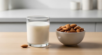 Vaso de leche de almendras y bowl con almendras crudas sobre mesa de madera en cocina iluminada