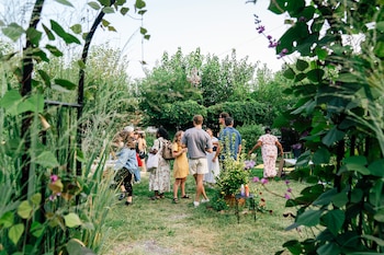 Grupo de personas en un jardín con mucha vegetación. Dos aerosoles sobre una mesa pequeña. Plantas con flores moradas y hojas verdes