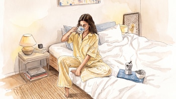 Ilustración en acuarela de una mujer en pijama amarillo sentada en una cama con una taza, una cafetera italiana y una mesa de noche.