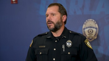 Hombre con uniforme de policía, insignia de Garland Police en el pecho y el brazo, barba, frente a un fondo azul con el logo institucional
