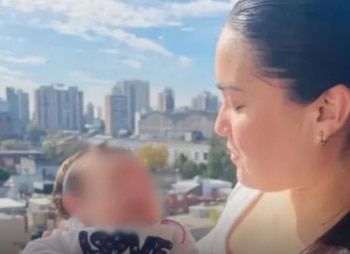 Una mujer de perfil sostiene a un bebé con el rostro pixelado frente a edificios urbanos y el cielo