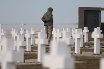 Un hombre de espaldas viste abrigo y camina entre hileras de cruces blancas en un cementerio