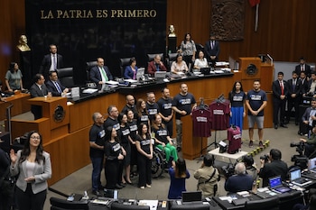 Grupo de personas en una sala legislativa. La mayoría viste camisetas "Yo con Mario". Camisetas "Morena Senado" cuelgan en percheros. Hay personas sentadas en mesas de trabajo.