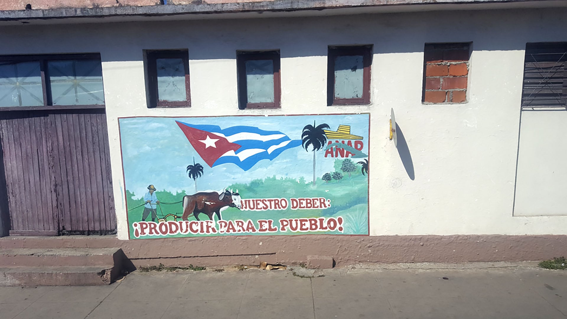 Un mural en una pared cubana representa un agricultor trabajando y la bandera nacional, con la frase: