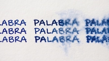 Papel blanco con textura, la palabra 'PALABRA' escrita en tinta azul tres veces, con tinta más difusa hacia la derecha