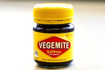 Frasco de vidrio oscuro con tapa amarilla y etiqueta con la palabra Vegemite sobre un fondo claro desenfocado