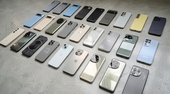 Múltiples teléfonos inteligentes de diversos colores y diseños alineados en varias filas sobre un suelo de cemento gris.