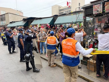 Agentes con chalecos de emergencia, policías con escudos protectores y una multitud detrás de una cinta amarilla en una calle comercial
