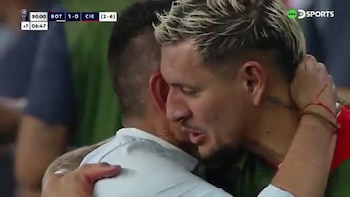 Un futbolista de cabello teñido de rubio abraza a un hombre con camisa blanca durante una transmisión deportiva