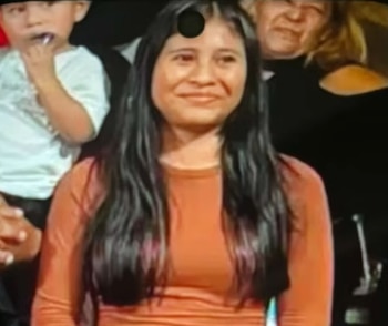 Retrato de una joven con cabello oscuro y largo, vestida con una camiseta naranja de manga larga, mirando al frente con una leve sonrisa
