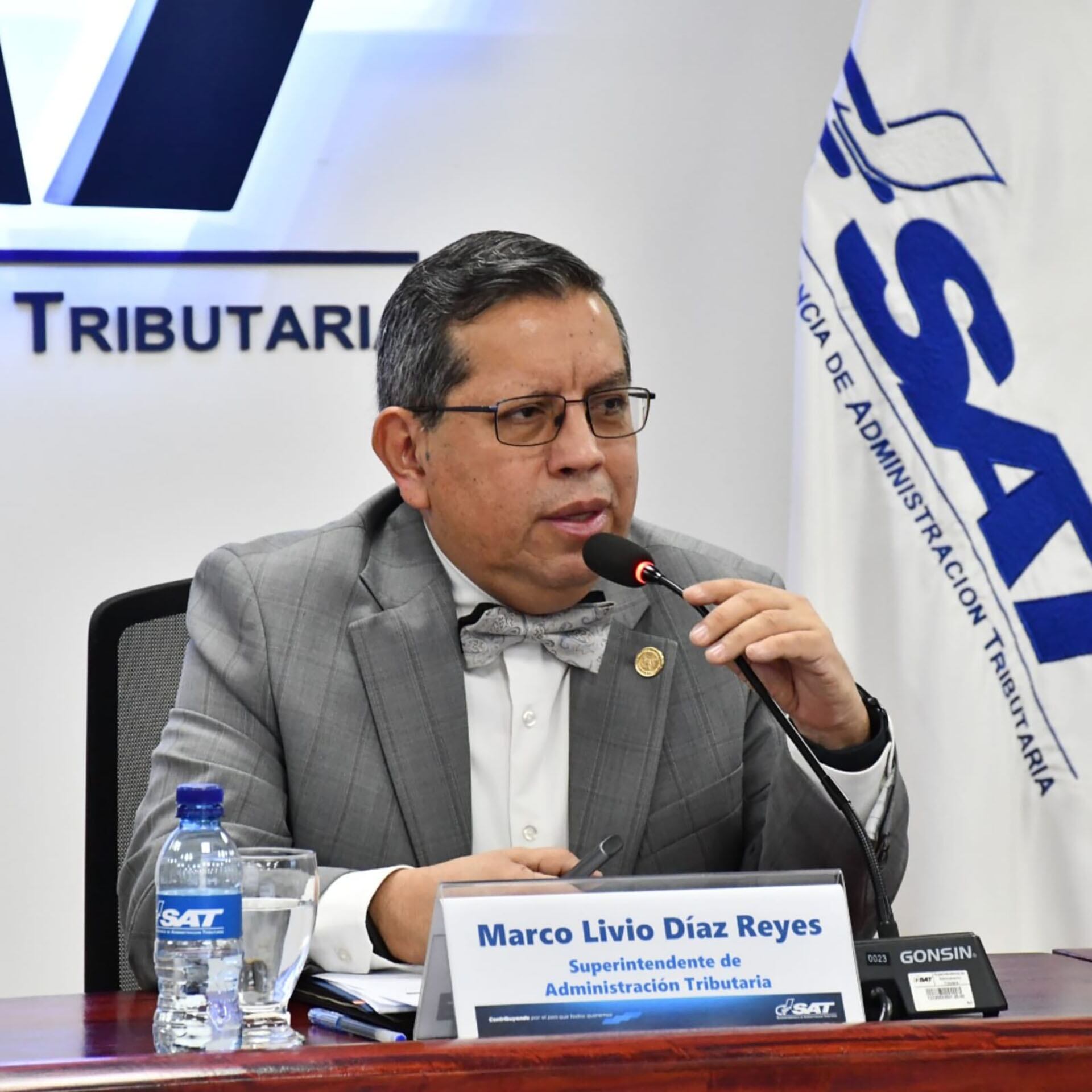 Foto de archivo para ilustrar: Marco Livio Díaz Reyes, Superintendente de Administración Tributaria de Guatemala, atiende a los medios de comunicación en un evento oficial, con el logo de la SAT visible al fondo. (Archivo de la SAT Guatemala)