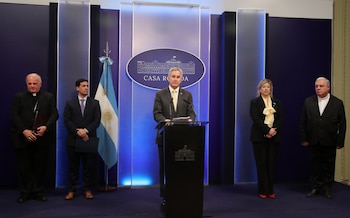 Un hombre habla tras un atril de la Casa Rosada junto a la bandera de Argentina, dos religiosos y dos personas con traje