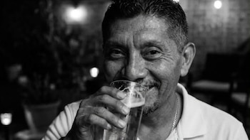 Retrato en blanco y negro de un hombre que sonríe mientras acerca un vaso de vidrio a sus labios