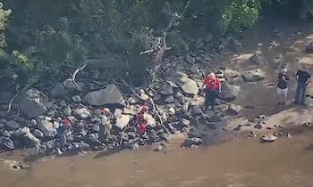 Vista aérea de rescatistas con uniformes de emergencia en la orilla rocosa de un río junto a una zona arbolada
