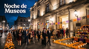 Personas vestidas con trajes y maquillaje de catrinas frente a un edificio colonial decorado con flores de cempasúchil, velas y papel picado.