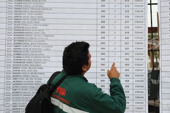 Un hombre de espaldas, vestido con una casaca verde con el logo de Petroperú, señala con el dedo índice una lista impresa de nombres y números