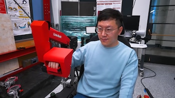 Un hombre con gafas y suéter azul sujeta una palanca de mando roja de la marca Link-Belt en un laboratorio