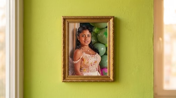 Cuadro pequeño con marco dorado en pared verde lima. El cuadro muestra el retrato de una mujer con vestido estampado y globos verdes y rosas.