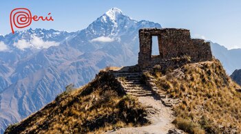 Ruinas de piedra en la cima de una colina con sendero, montañas nevadas y valles al fondo, cielo azul claro, y logo rojo de Perú en la esquina superior izquierda.