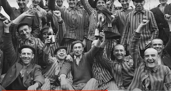 Grupo de hombres sonrientes y jubilosos, algunos con uniformes a rayas de prisión, levantando los brazos y botellas en celebración, en blanco y negro