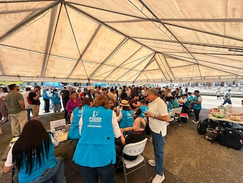 Un grupo de personas bajo una carpa, varias con chalecos azules de "Poder Ciudadano Guatemala", interactúan alrededor de mesas con objetos