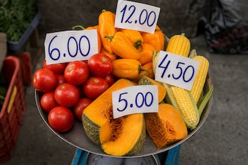 Tomates, pimientos, choclos y trozos de zapallo sobre una balanza metálica con carteles de papel que muestran números.