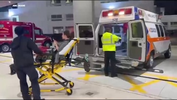 Un socorrista empuja una camilla con un paciente hacia una ambulancia con las puertas traseras abiertas