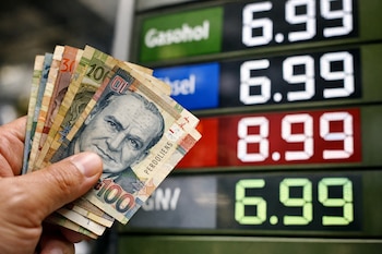 Una mano sujeta billetes de cien, veinte y diez soles peruanos delante de una pantalla que muestra los precios de gasohol, diésel y GNV.