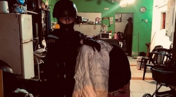 Agente uniformado con casco y una mujer cubierta en el interior de una casa con paredes verdes, refrigerador y un cochecito de bebé