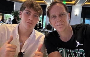 Dos hombres, uno joven y otro adulto, en primer plano. El joven con camisa clara, el adulto con camiseta oscura. Ambos hacen un gesto de pulgar hacia arriba. Fondo de restaurante