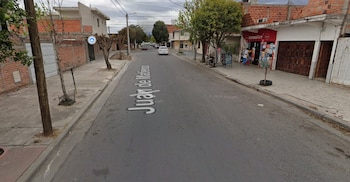 Una calle asfaltada con casas de ladrillo, aceras, árboles, un automóvil blanco al fondo y un local comercial a la derecha