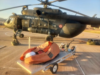 Un helicóptero militar de la Fuerza Aérea del Perú estacionado en una pista con un sistema helibalde sobre un remolque en primer plano