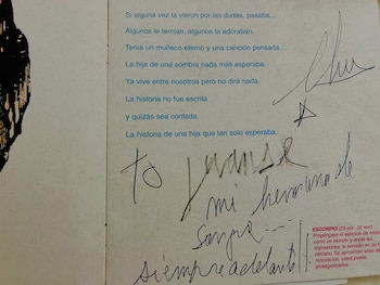 Primer plano de una página con texto impreso en azul y una dedicatoria escrita a mano en tinta negra, con la firma de Charly García al margen