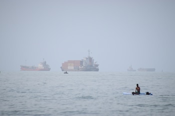 ARCHIVO - Un hombre se sienta en una tabla de surf con un barco portacontenedores al fondo junto a otros buques comerciales, en el estrecho de Ormuz, desde Bandar Abbas, irán, el lunes 27 de julio de 2026. (Razieh Poudat/ISNA via AP, Archivo)