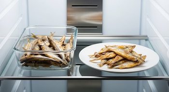 Interior de una heladera moderna que contiene un recipiente de vidrio con cornalitos cocidos y un plato blanco con cornalitos cocidos.