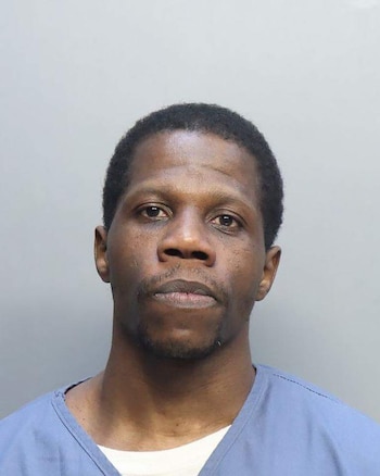 Primer plano de un hombre afroamericano con cabello oscuro y corto, y barba ligera, mirando al frente. Viste una camisa azul sobre una camiseta blanca