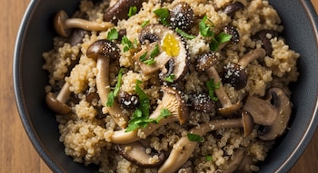 Cuenco oscuro con quinoa, varios tipos de hongos, perejil picado y espolvoreado blanco sobre una superficie de madera clara.