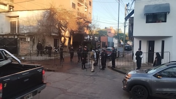 Oficiales de policía en uniforme negro y barreras metálicas en una calle urbana. Un SUV gris y una camioneta pickup negra son visibles