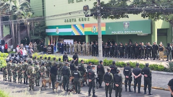 Miembros de la policía formados en filas junto a perros adiestrados frente a un edificio oficial con banderas y letreros