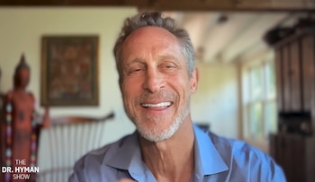 Primer plano de un hombre sonriente con camisa azul en una habitación con un cuadro y una figura decorativa al fondo