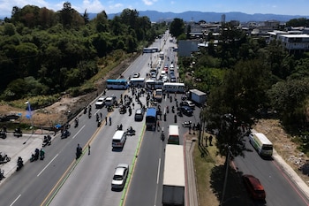 Vista aérea de una carretera bloqueada por autobuses atravesados, automóviles detenidos y personas reunidas en el centro de la vía.
