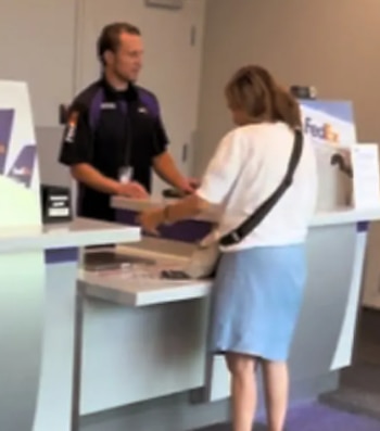 Un hombre con uniforme negro y morado atiende a una mujer con camiseta blanca y falda azul en un mostrador de servicio con un logo de FedEx