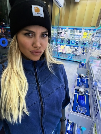 Wanda Nara posa para una selfie en un local de juegos, vistiendo un gorro negro y una chaqueta azul, con varias máquinas recreativas de fondo