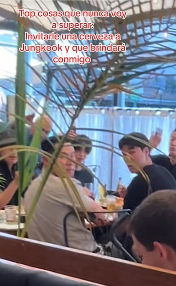 Un grupo de personas sentadas a la mesa en un restaurante detrás de una planta con un texto superpuesto en la parte superior